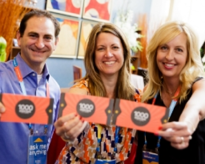 Three smiling individuals hold up orange badges with the text 